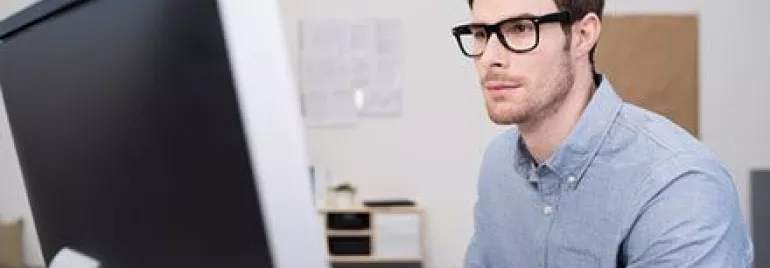 Homem de óculos trabalha em computador em escritório.