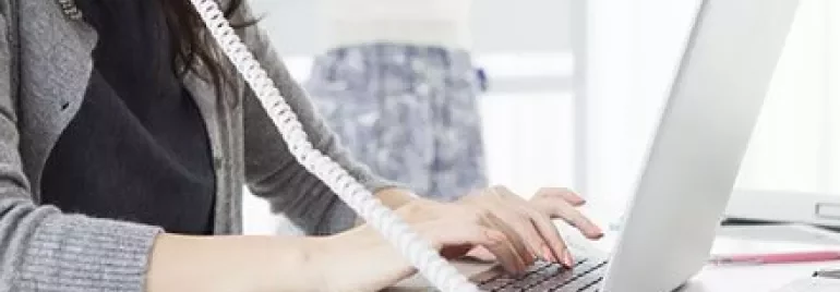 Mulher digitando no laptop, usando telefone no escritório.