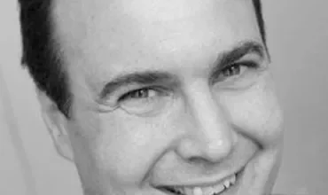 Homem sorrindo em uma foto em preto e branco.