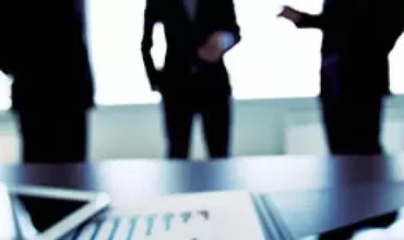 Três pessoas discutindo em uma sala de reunião ofuscada.