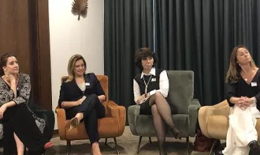 Quatro mulheres sentadas em poltronas em uma sala de reuniões.