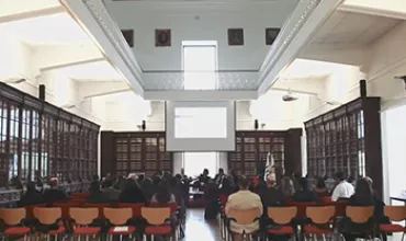 Pessoas assistindo a uma apresentação em uma sala de conferência com cadeiras coloridas.