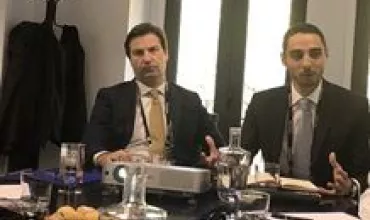 Dois homens de terno em reunião com aparelho de projeção na mesa.