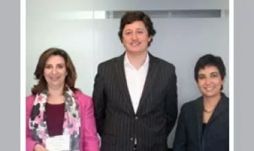 Três pessoas sorrindo para a foto em um ambiente corporativo.