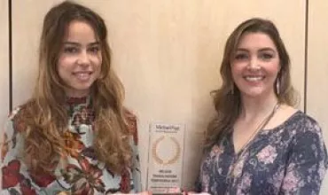 Duas mulheres segurando um troféu em frente a um fundo de madeira.
