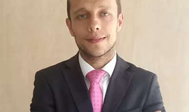 Homem de terno cinza e gravata rosa com braços cruzados.