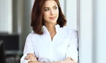 Mulher em pé com camisa branca, braços cruzados.