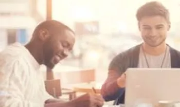 Dois homens sorrindo enquanto trabalham em um laptop em um café.
