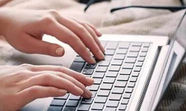 Mãos digitando em um laptop prateado.