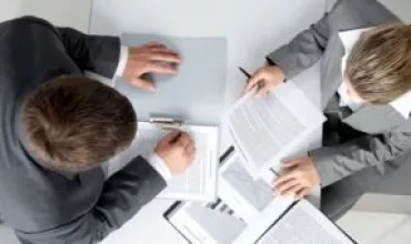 Duas pessoas de terno revisando documentos em uma mesa.