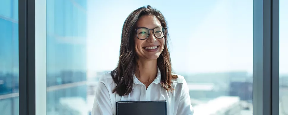 Mulher sorridente com óculos e cabelo castanho em escritório moderno.
