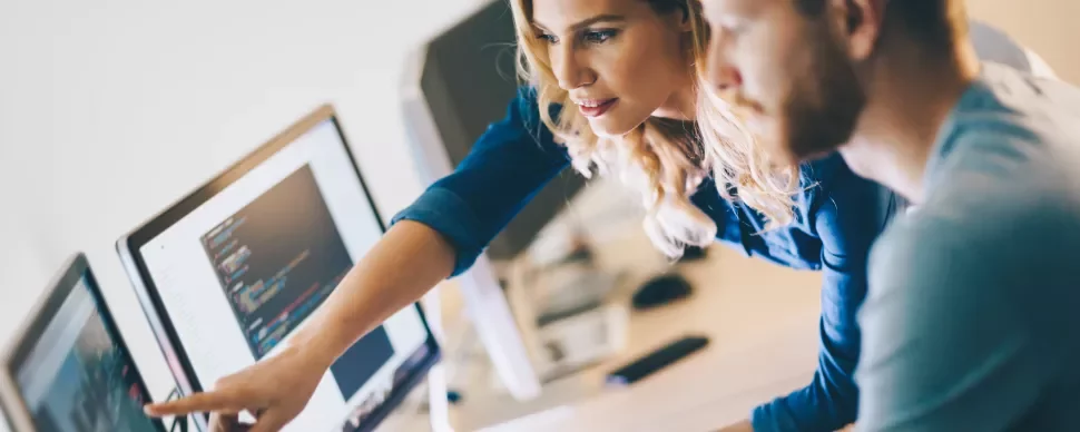 Dois colegas analisam código na tela do computador.