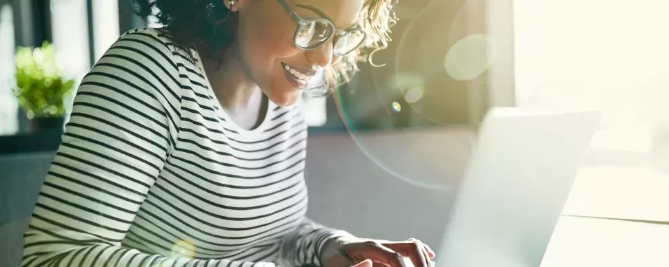 Mulher sorrindo trabalhando em laptop com luz do sol