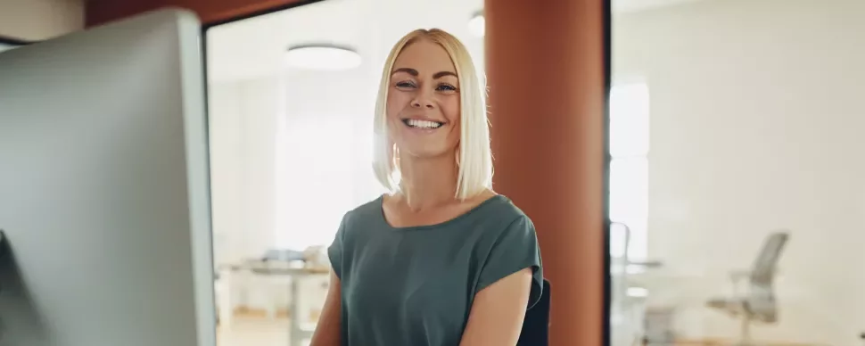 Pessoa sorrindo em frente a um computador em um escritório.