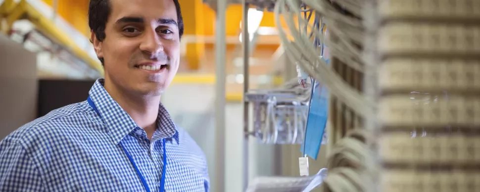 Homem sorrindo em sala de servidores com cabos ao fundo.