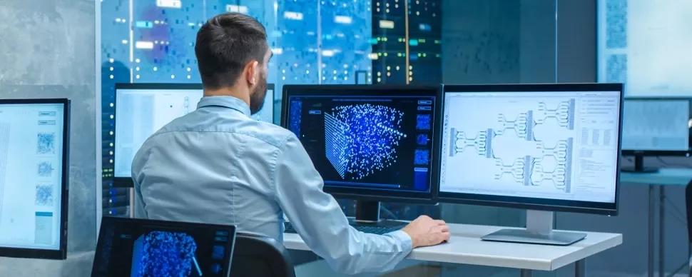 Profissional analisa dados em múltiplos monitores na sala de servidores.