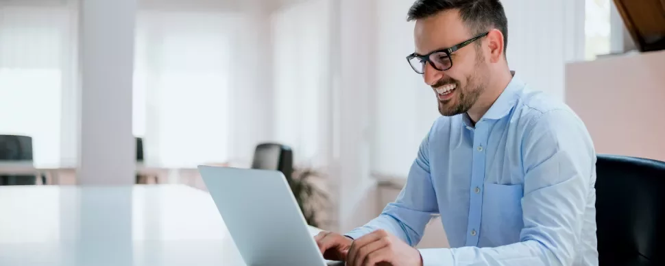 Homem sorridente usando laptop em escritório.