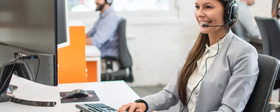 Mulher de fone de ouvido atendendo cliente ao computador.
