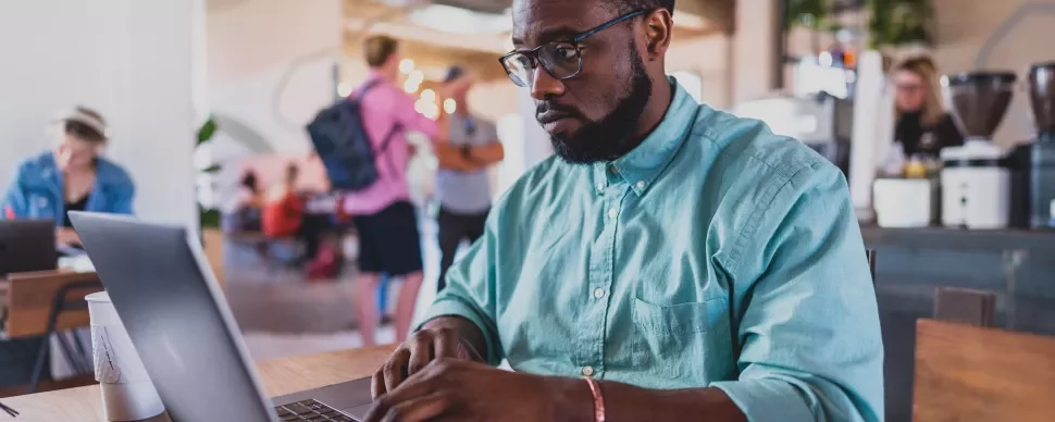 Homem com camisa verde trabalha em um laptop em um café.