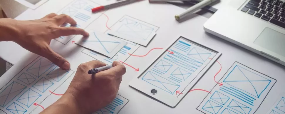 Pessoa criando design de interface em papel com laptop.