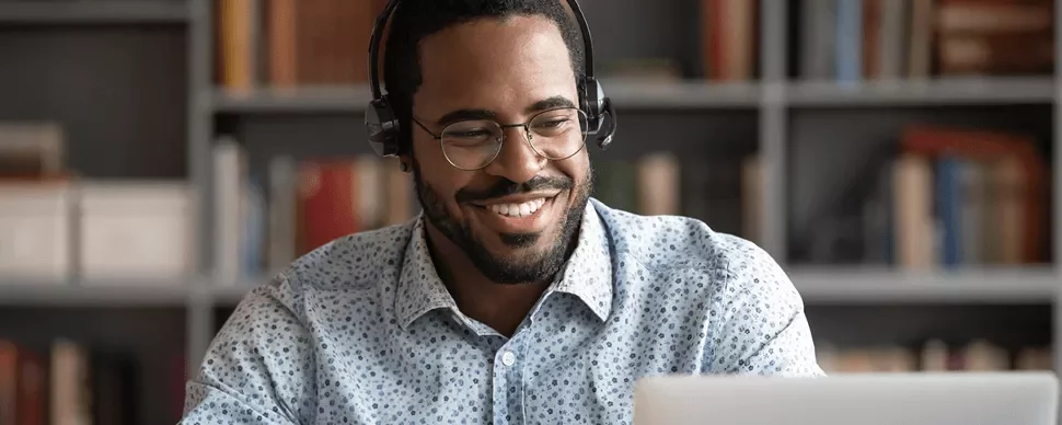 Homem sorrindo usando fones de ouvido, olhando para o laptop.