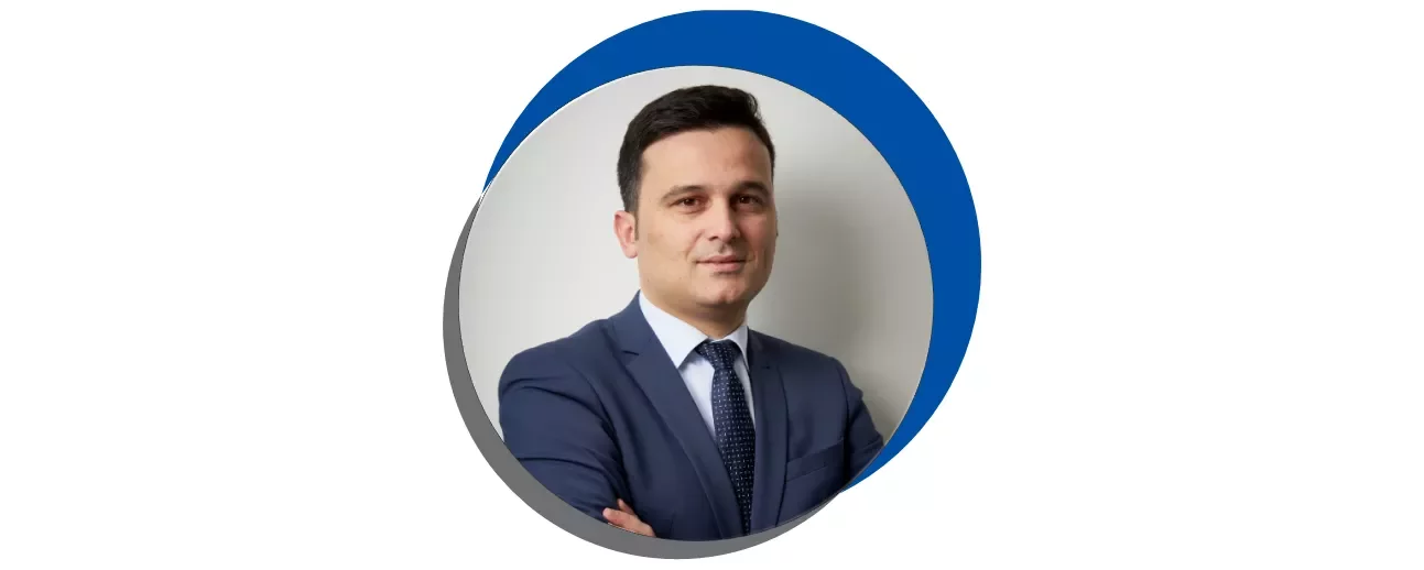 Homem de terno azul em retrato circular com fundo azul e cinza.