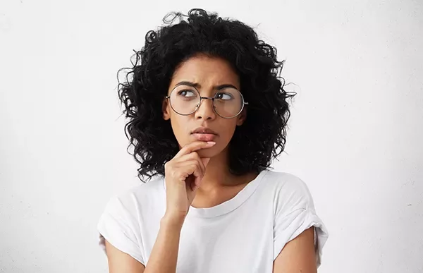 Mulher de óculos pensando, mão no queixo.