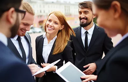 Grupo de pessoas em ternos sorrindo e conversando ao ar livre.