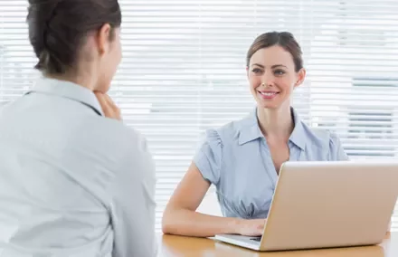 Duas mulheres conversando em um escritório com laptop.