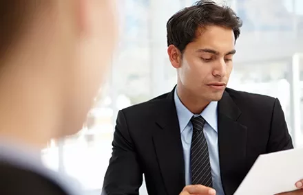 Homem de terno examinando documento em reunião.
