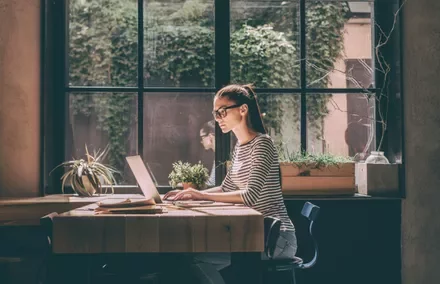 Mulher trabalhando em laptop em um café iluminado pelo sol.