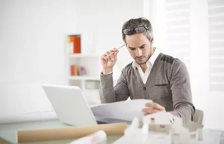 Homem analisando documentos em frente ao laptop.