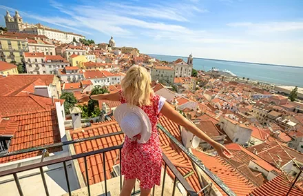 Mulher com chapéu admirando a vista panorâmica de uma cidade costeira ensolarada.