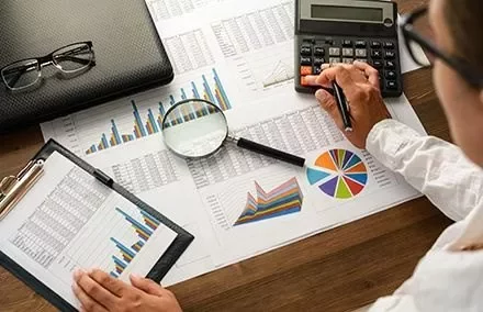 Pessoa analisando gráficos e fazendo cálculos com uma calculadora.