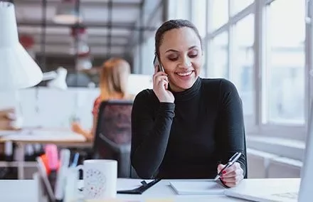 Mulher sorrindo ao telefone em um escritório moderno.