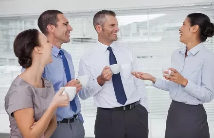 Grupo de colegas conversando e sorrindo durante uma pausa para o café.