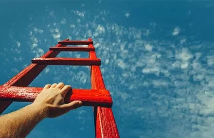 Mão segurando uma escada vermelha contra o céu azul.