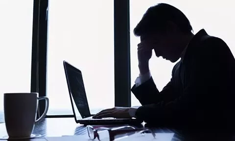 Homem preocupado sentado em frente ao laptop.