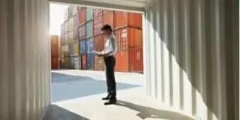 Homem de pé em um contêiner, verificando documentos.