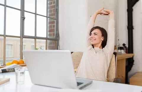 Mulher sorrindo e espreguiçando-se em frente ao laptop.
