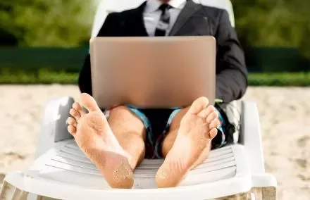 Homem de terno trabalhando em um laptop sentado na praia.