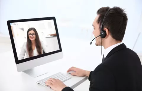 Homem com fone de ouvido em videoconferência com mulher em computador.